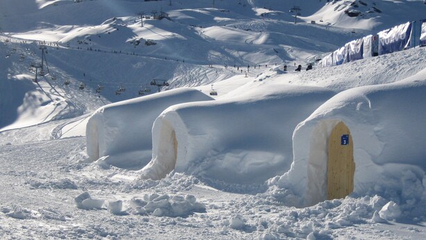Paisagem coberta de neve com iglus e um teleférico ao fundo.