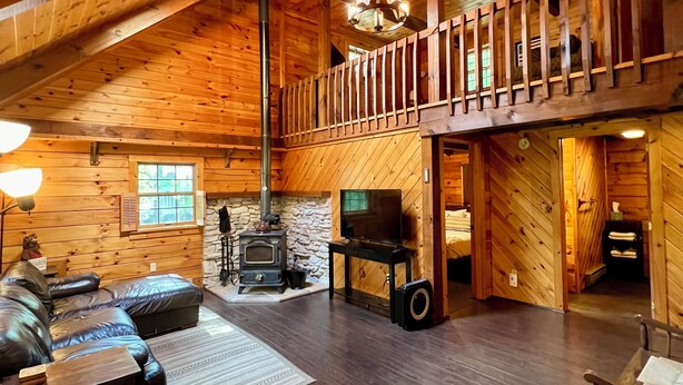 Ein geräumiges Blockhaus-Interieur mit hohen Decken, Kamin, Fernseher und einer gemütlichen Sitzecke.