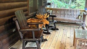 Eine Blockhütte mit einer Holzveranda, komplett mit Schaukelstühlen, einem Tisch und einem Glastisch.