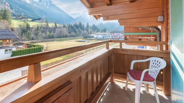 A wooden balcony with a view of a mountain landscape, a chair, and a building in the background. - Apartment in Wald Near Zillertal Ski Area (Wald im Pinzgau)