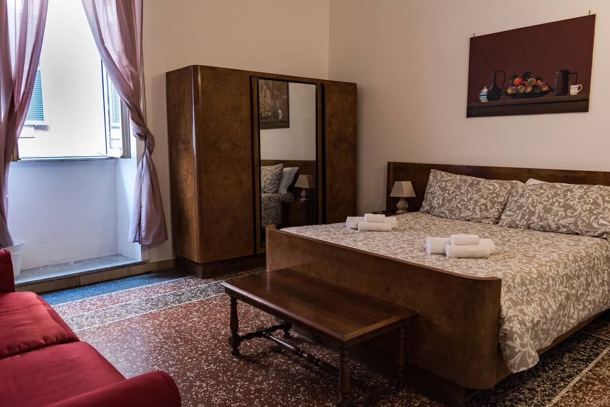 A hotel room with a large bed, a wooden bench, a wardrobe, and a painting on the wall.