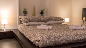 Une chambre à coucher avec un grand lit, deux tables de chevet avec des lampes, une petite plante en pot et un téléviseur fixé au mur.