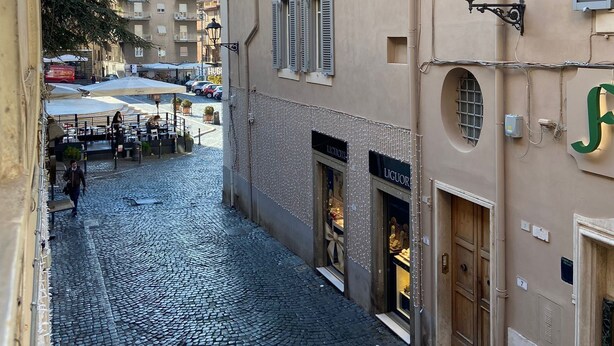 Une rue pavée bordée de bâtiments des deux côtés, avec une boutique dont l’enseigne indique « BOISSONS ALCOOLISÉES ».
