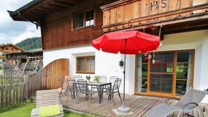 A wooden house with a patio area featuring a table and chairs, a red umbrella, and a wooden deck. - Chalet in Leogang Near Ski Slopes (Leogang)