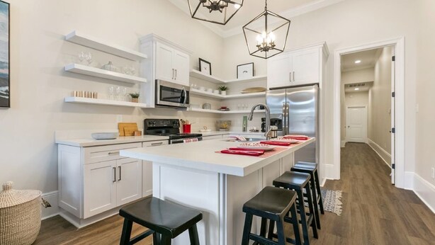 Una cocina moderna con armarios blancos, una isla central con taburetes, un refrigerador de acero inoxidable y un microondas.