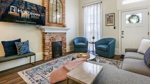 Una sala de estar con chimenea, un televisor montado en la pared y dos sillones azules.