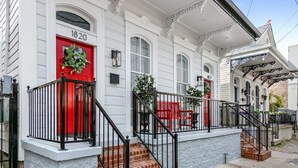 Un edificio blanco con puerta roja, número 1820, y barandilla de metal negro.