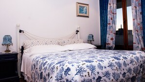Une chambre à coucher avec un lit, deux tables de chevet, une commode, un tableau encadré au mur et une fenêtre avec des rideaux.