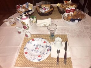 Ein Frühstückstisch mit verschiedenen Speisen, darunter Brot, Gebäck und Würzmitteln.
