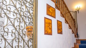 Un escalier avec des marches en bois et une moquette bleue, menant à un palier avec un mur blanc et trois tableaux encadrés.