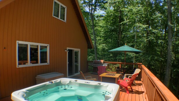 Una terraza de madera con un jacuzzi, mobiliario exterior y una zona de estar cubierta.