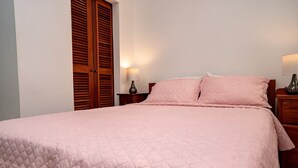 A neatly made bed with a pink quilt, wooden headboard, and two bedside lamps. - The Orchid Studio Experience" (Caye Caulker)