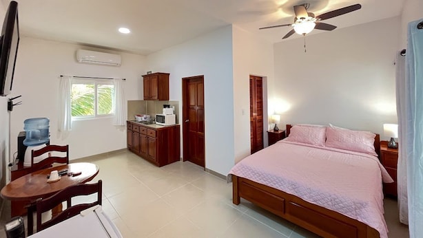 A bedroom with a bed, bedside tables, a ceiling fan, and a window. - The Orchid Studio Experience" (Caye Caulker)