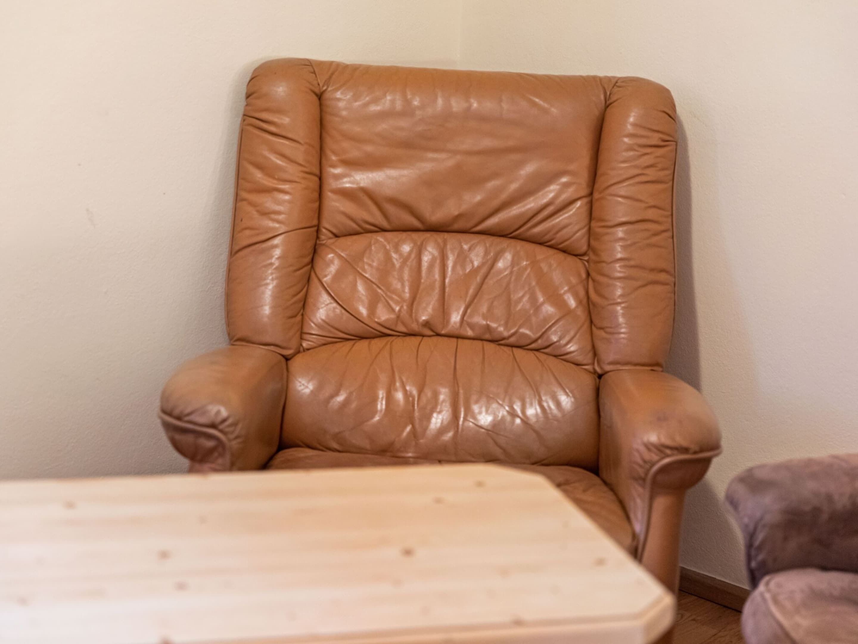 A tan leather armchair with a high backrest and armrests, positioned against a plain wall.
