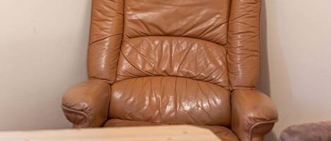 A tan leather armchair with a high backrest and armrests, positioned against a plain wall.