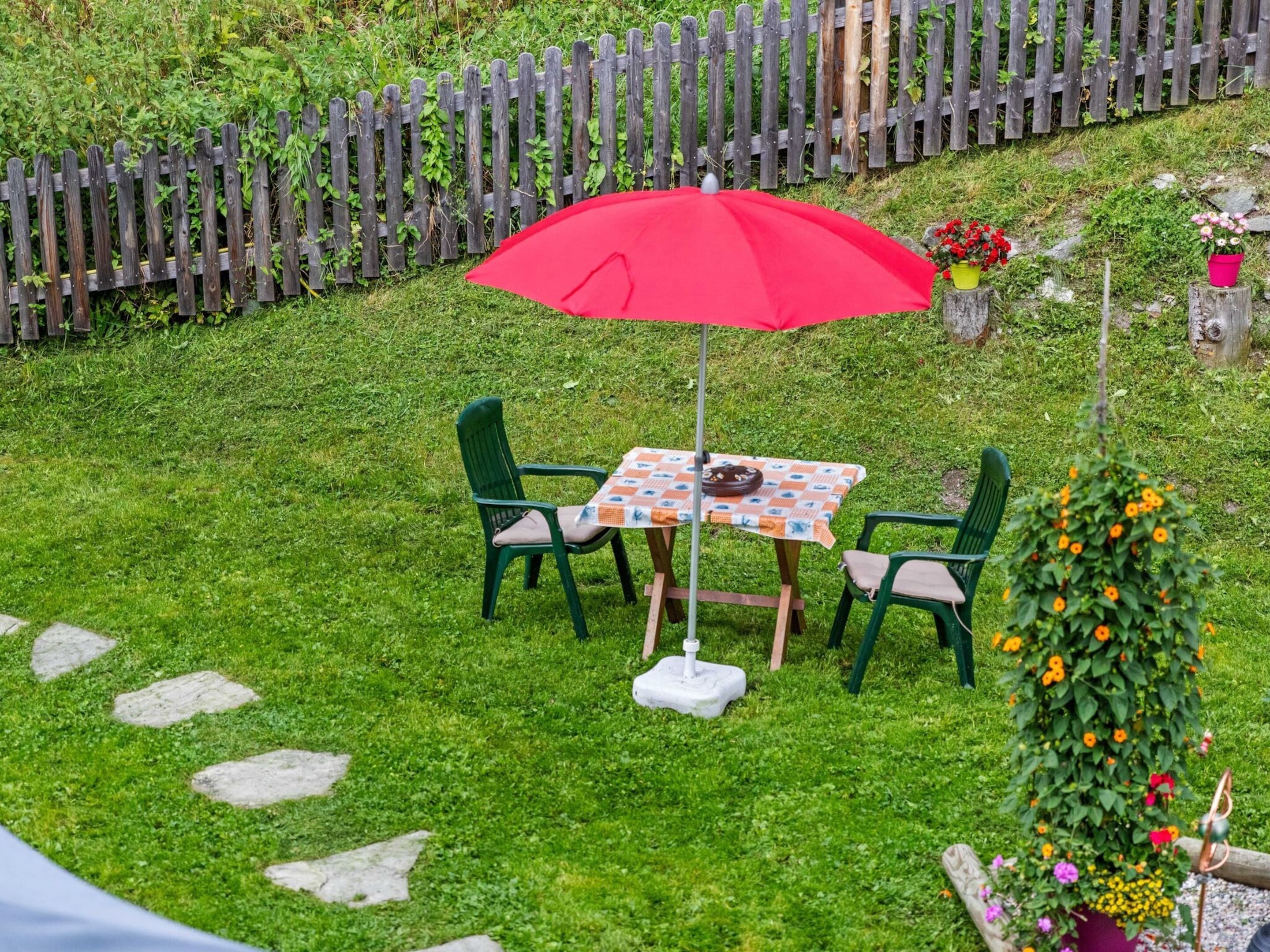 Een terras met een tafel en stoelen, een rode parasol en een houten omheining op de achtergrond.