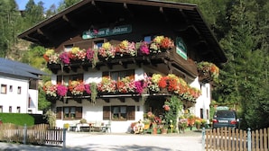 A traditional Alpine-style building with multiple balconies adorned with colorful flowers, a sign indicating a restaurant, and a wooden fence in the foreground. - Spacious Apartment in Salzburg near Ski Area (Saalbach-Hinterglemm)