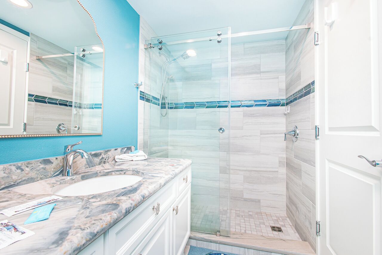 A bathroom with a glass-enclosed shower, a marble sink, and a large mirror.