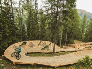 A wooden bike ramp in a forested area with trees and mountains in the background.