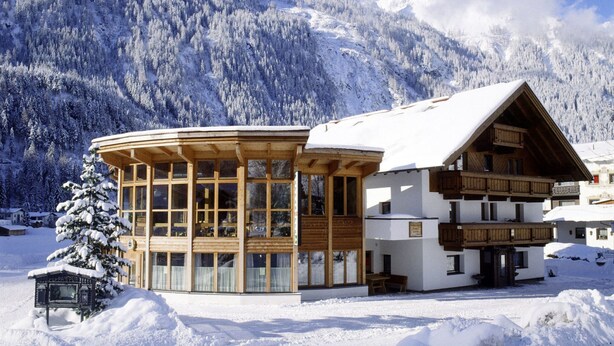 A wooden chalet with large windows, a snow-covered roof, and a mountain backdrop. - Sunlit Apartment near Ski Area in Längenfeld (Laengenfeld)
