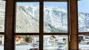 A room with large windows offering a view of snow-covered mountains and a small town below. - Sunlit Apartment near Ski Area in Längenfeld (Laengenfeld)