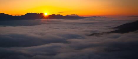 A sunrise over mountains with clouds below.