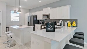 A modern kitchen with white cabinetry, a central island, bar stools, pendant lighting, and a bag labeled 'Master Vacation Homes' on the island. - 2 Bedrooms / 2 Bathrooms / Storey Lake (3120-403 PC) (Kissimmee)