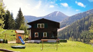 Un chalet en bois doté d’un balcon, d’un toboggan et d’un court de tennis, situé dans une région montagneuse.