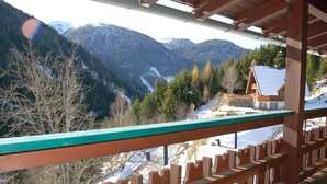 Un balcon en bois offrant une vue sur un paysage montagneux et une maison dont le toit est recouvert de neige.