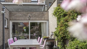 A patio with a wooden table and chairs, a sliding glass door, and a brick wall with climbing plants. - Vintage Villa in Knokke-Heist near Beach (Knokke-Heist)