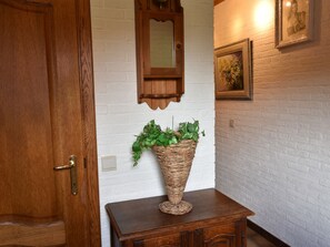 Une porte en bois, un mur en briques blanches, un miroir, un panier en osier rempli de plantes et un tableau encadré.