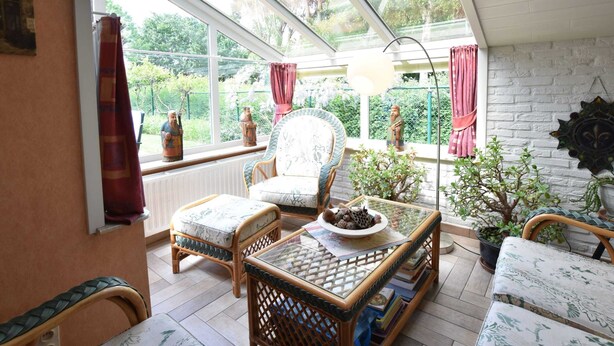 A sunlit room with wicker furniture, a glass table, and a view of greenery outside. - Family Home Close to the Beach (Bredene)
