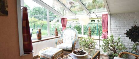 A sunlit room with wicker furniture, a glass table, and a view of greenery outside.