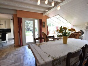 Un coin repas avec une table dressée pour quatre personnes, une plante en pot et une vue sur l’extérieur à travers une porte vitrée.