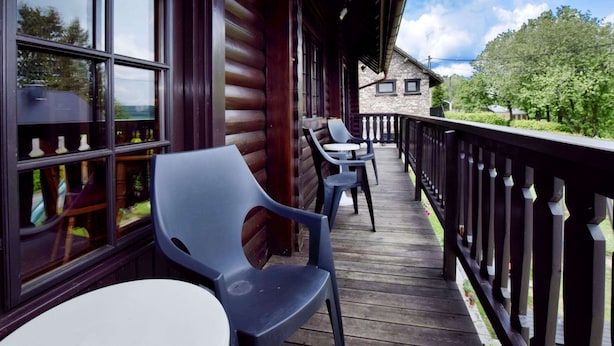 Une terrasse en bois avec des chaises et une table en plastique, donnant sur un jardin et un bâtiment en pierre.