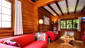 L’intérieur d’un chalet confortable, avec un canapé rouge, une table basse en bois et un téléviseur fixé au mur.