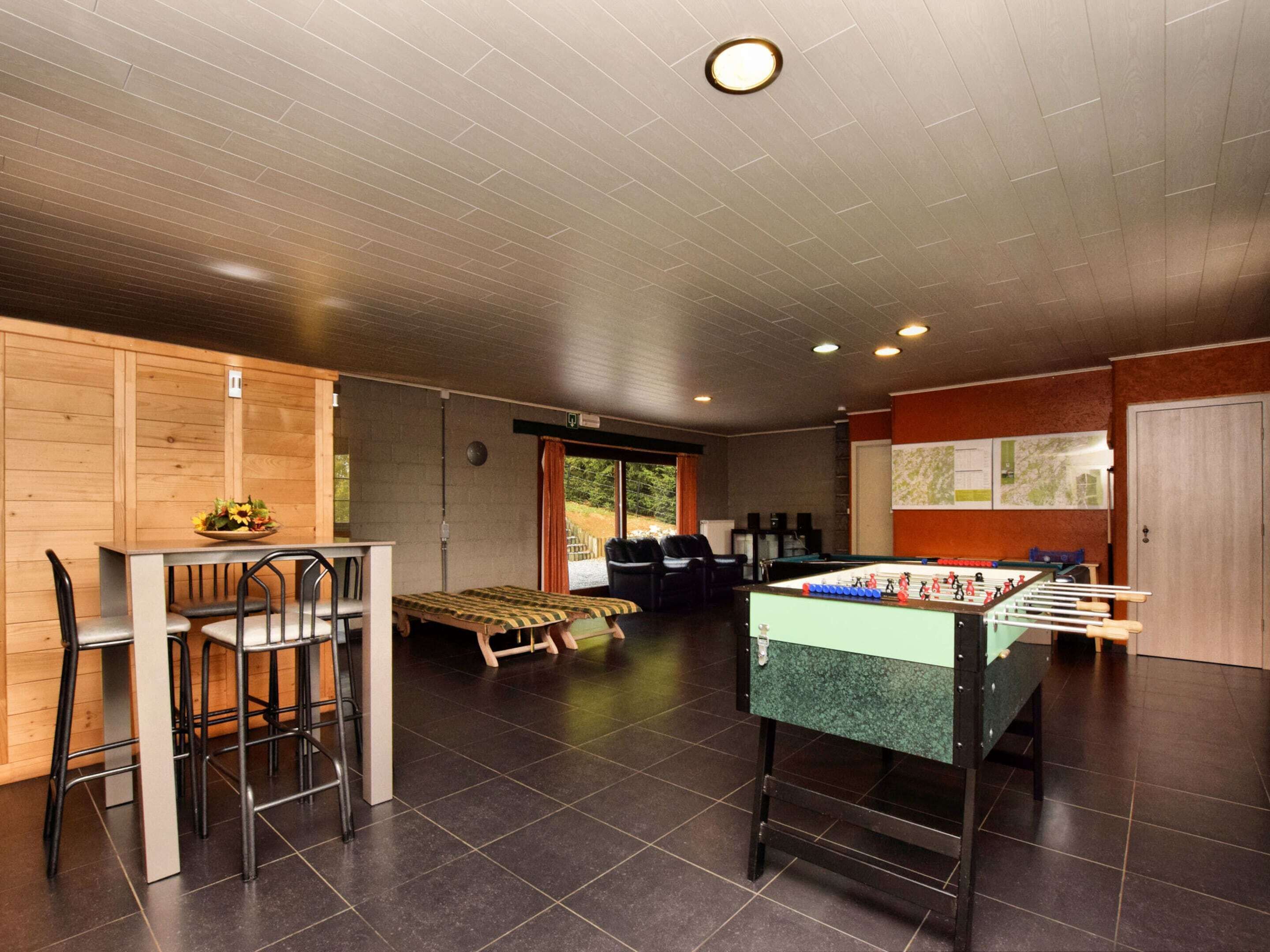 A room with a foosball table, a dining table with chairs, a bed, and a window with a view of greenery.