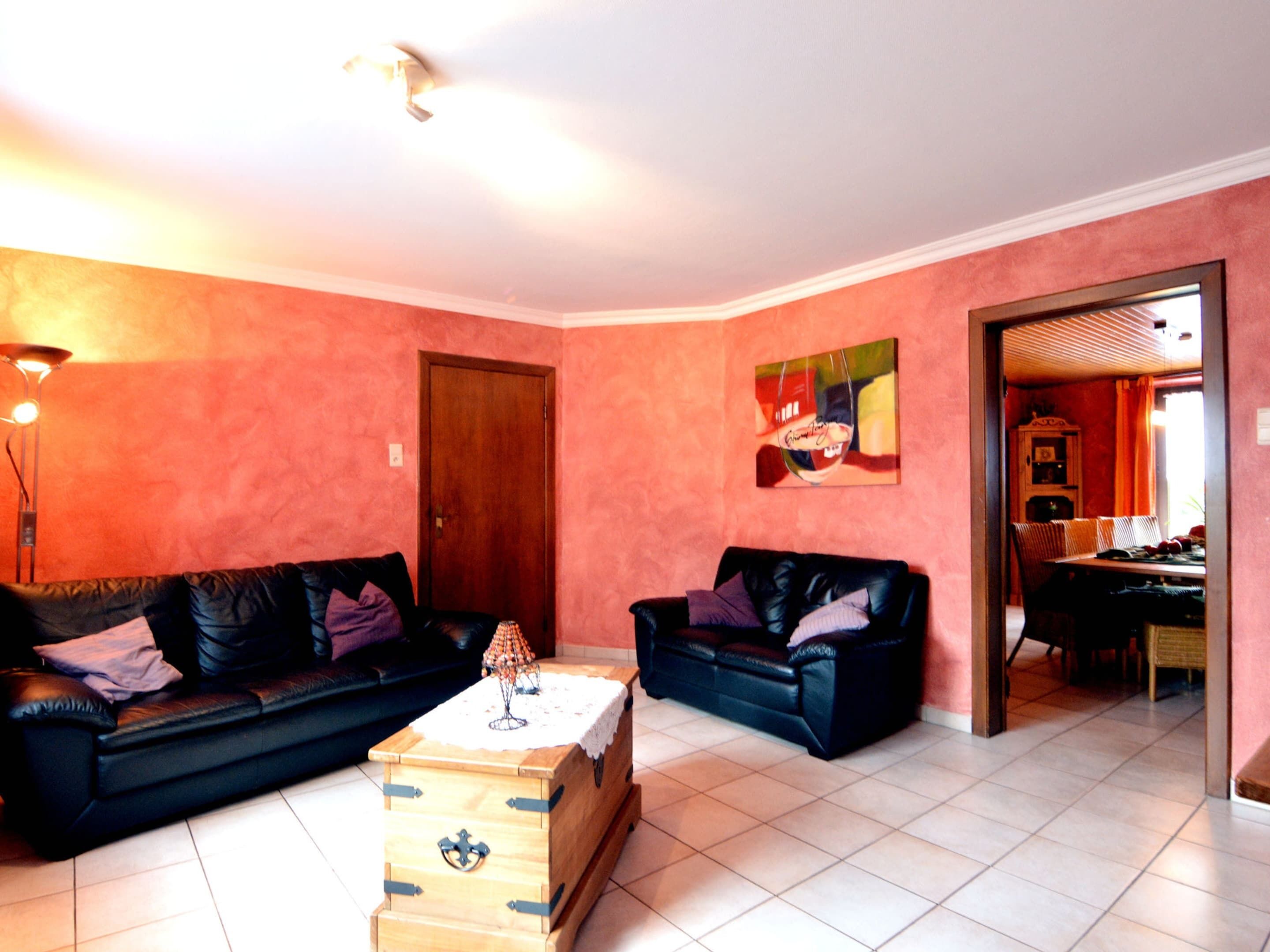 A living room with two black leather sofas, a wooden chest of drawers, and a painting on the wall.