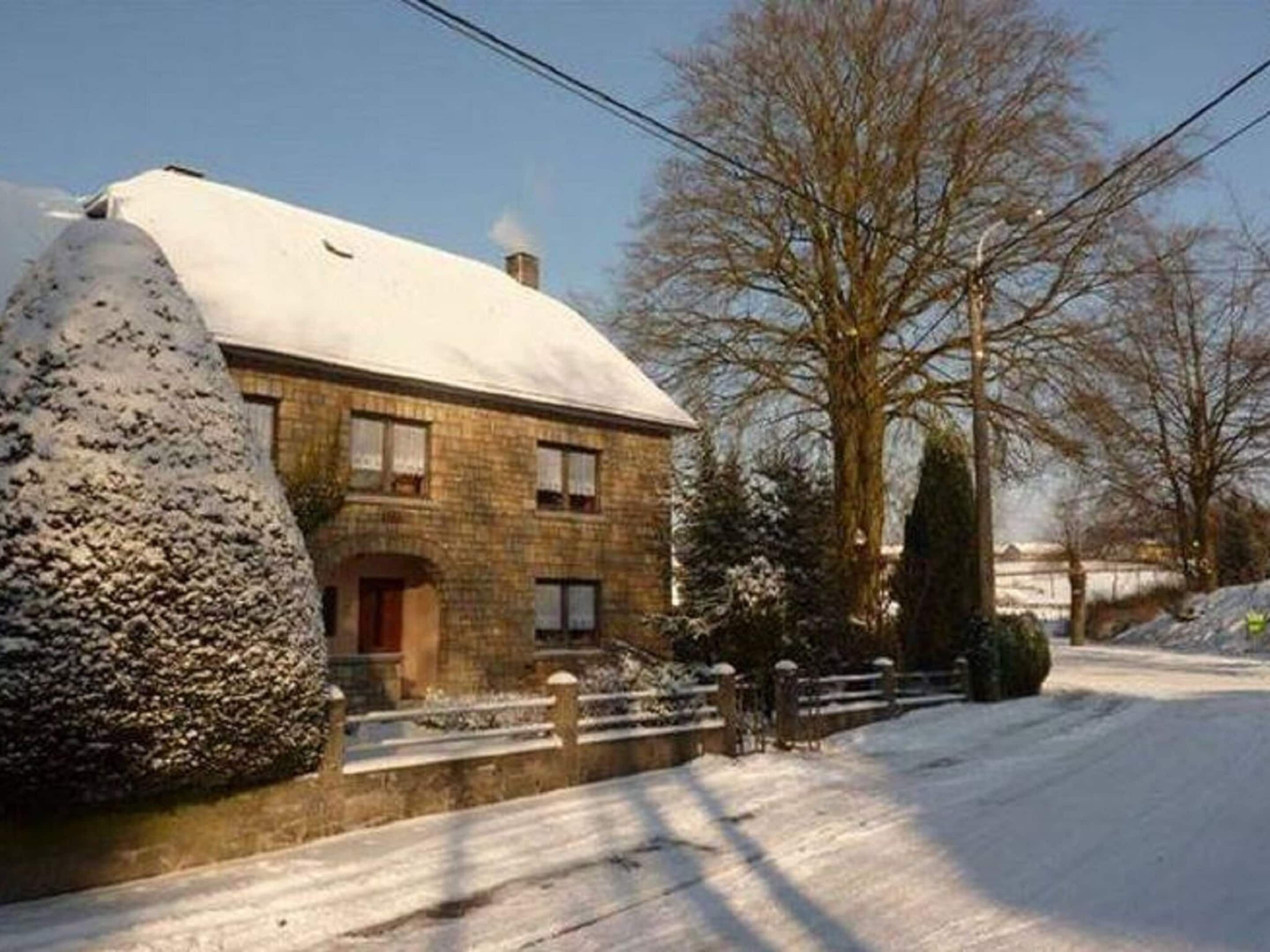 Una casa de piedra de dos pisos con techo nevado y un pequeño porche.