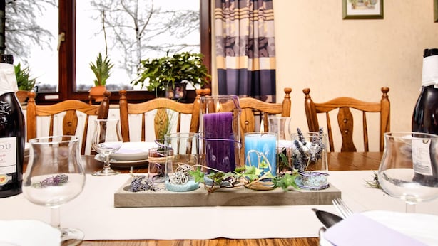 Un tavolo da pranzo apparecchiato con bottiglie di vino, bicchieri e candele, circondato da sedie di legno.