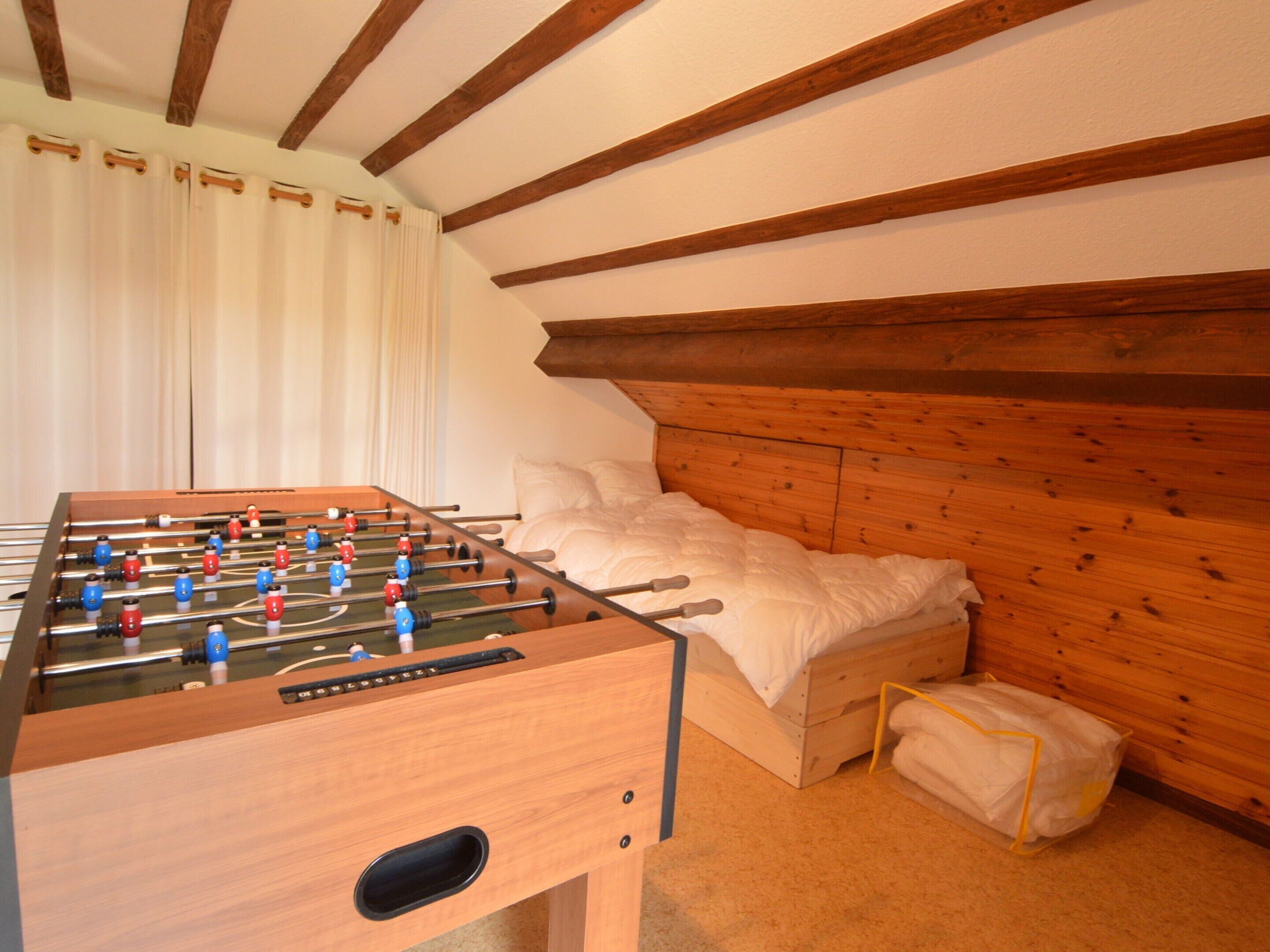 Una habitación con techo de madera, cama con ropa de cama blanca y una mesa de fútbol de mesa.