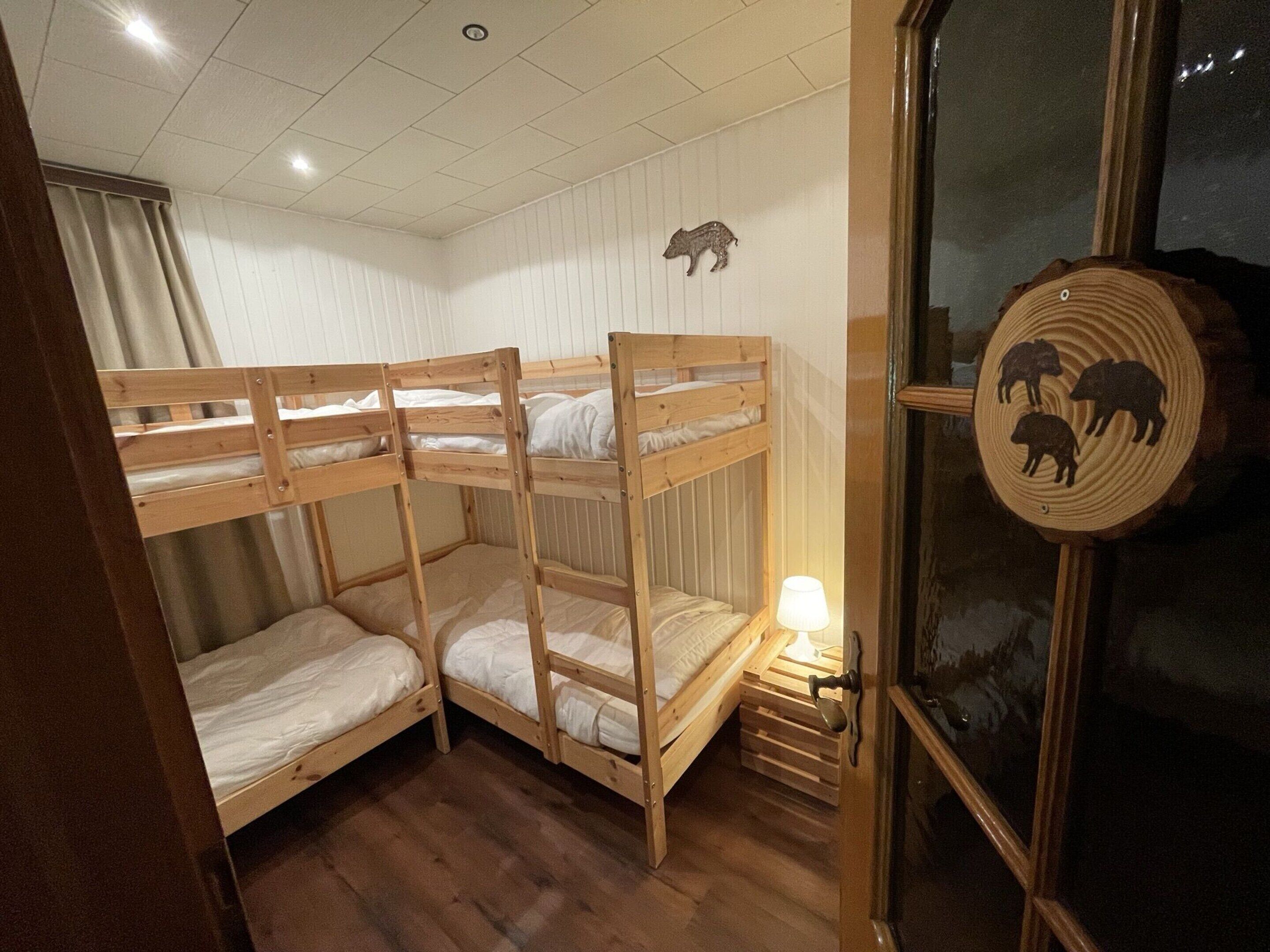 A room with three bunk beds, wooden walls, a window with a wooden door, and a wall-mounted animal decoration.