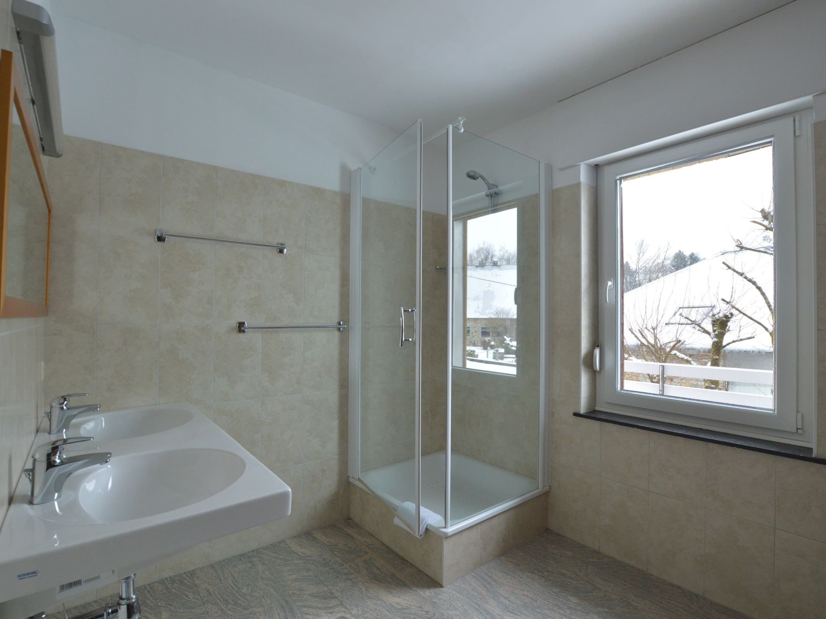 Ein modernes Badezimmer mit einer gläsernen Duschkabine, einem Waschbecken inklusive Spiegel und einem Fenster mit Blick nach draußen.