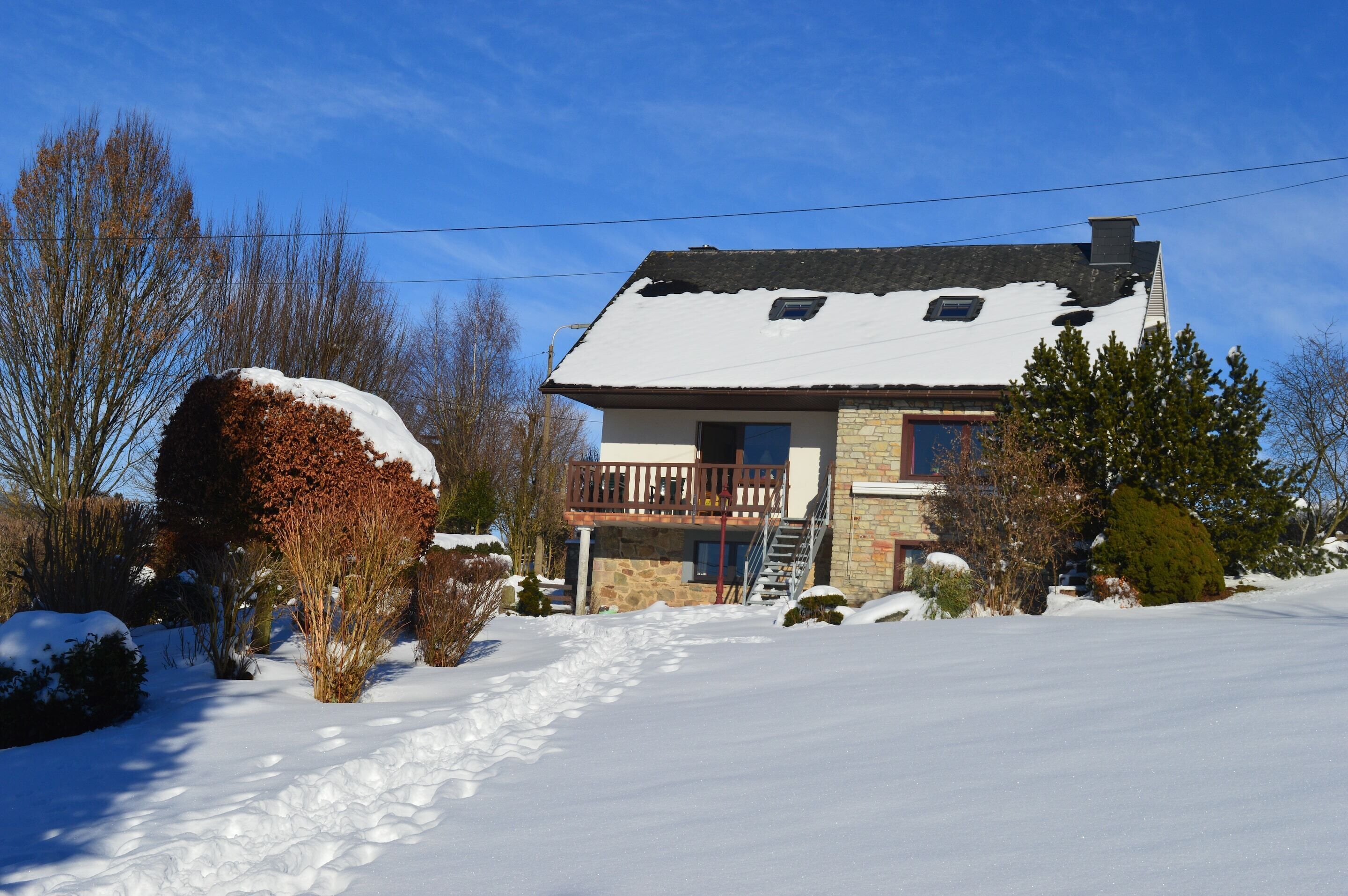Een tweelaags huis met een balkon, omringd door sneeuw bedekte grond en bomen.