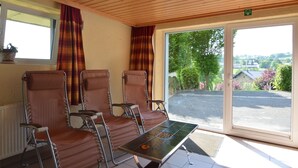 A room with four brown leather chairs, a small table with a decorative tile, a window with curtains, and a view of a parking lot and greenery outside. - Ondenval Stay With Sauna (Waimes)
