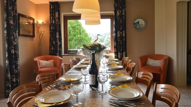 A dining room with a long table set for a meal, chairs, a vase with flowers, and a window with a view of greenery. - Ondenval Stay With Sauna (Waimes)