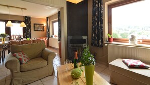 A living room with a sofa, a table with a vase and glasses, a fireplace, and a window with curtains. - Ondenval Stay With Sauna (Waimes)