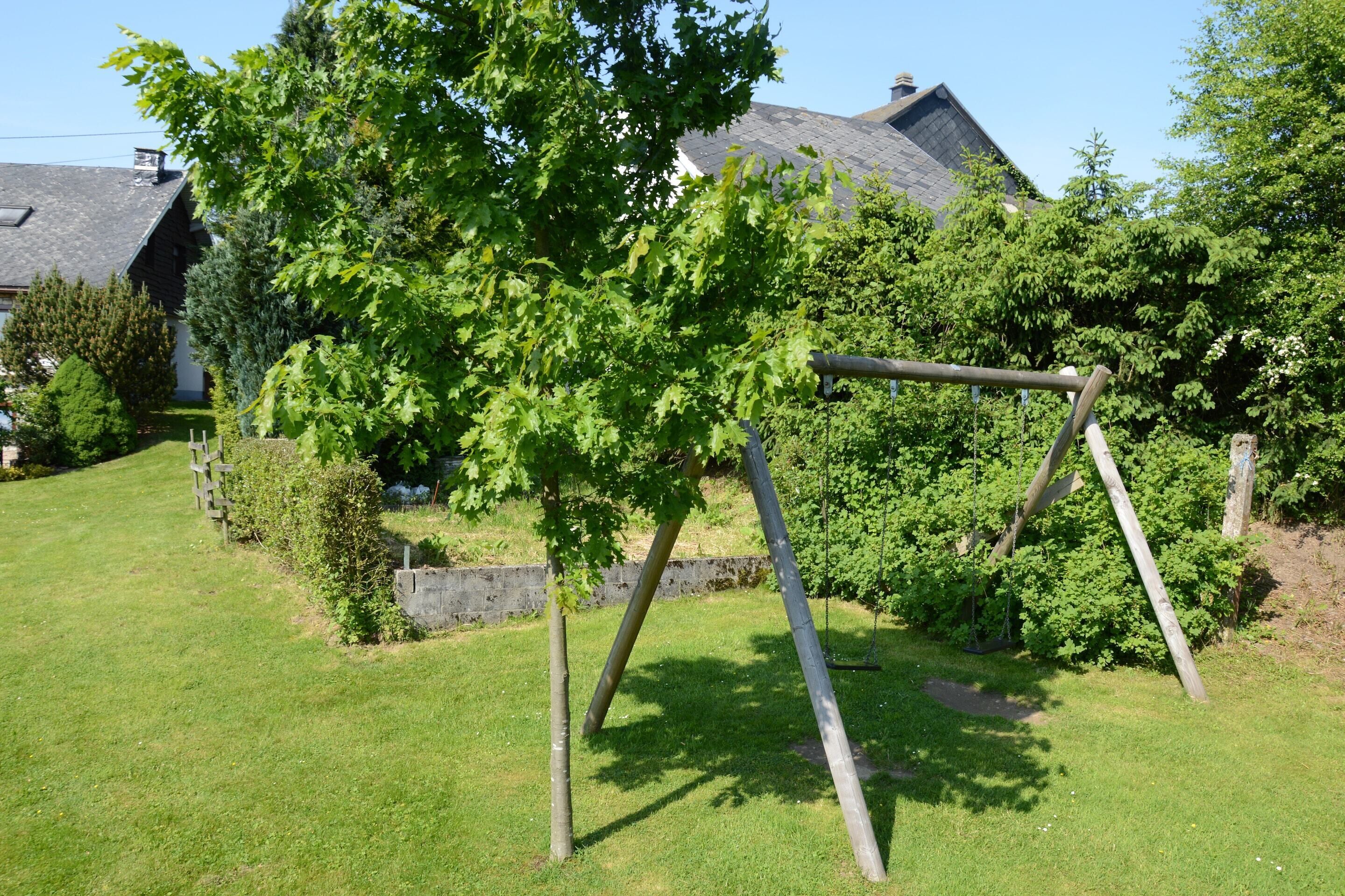 A grassy area with a swing set, trees, and a house with a sloped roof.