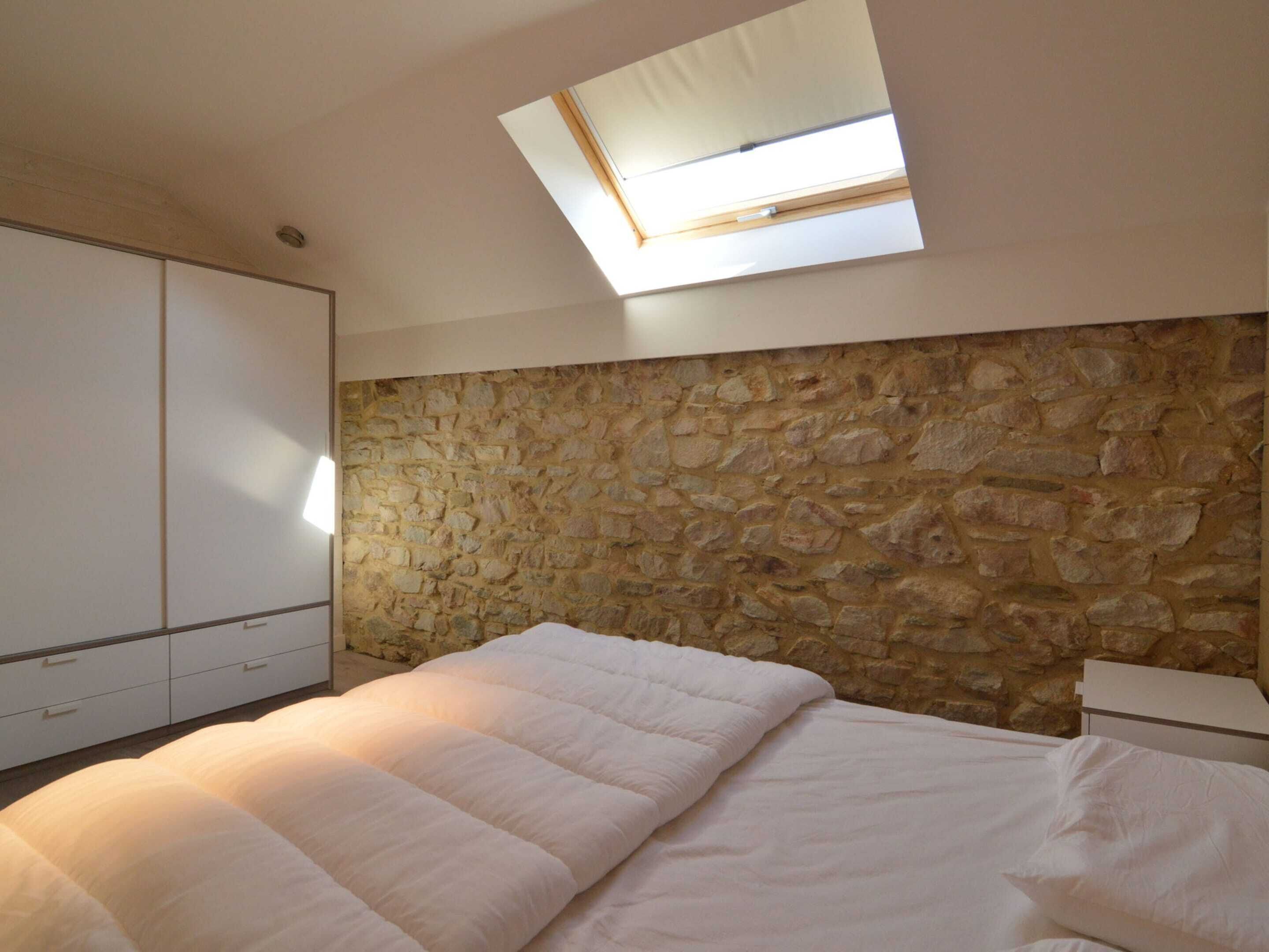 Ein Schlafzimmer mit Steinwand, Dachfenster, Bett und Kleiderschrank.