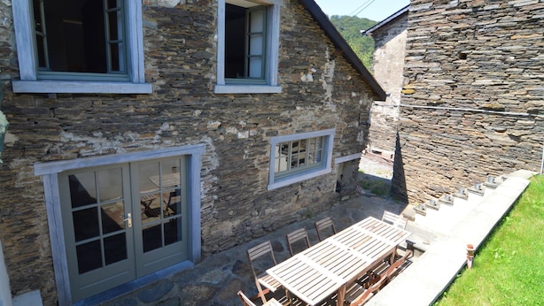 A stone building with a patio area featuring a wooden table and chairs. - Cozy Cottage Near River (Vresse-sur-Semois)
